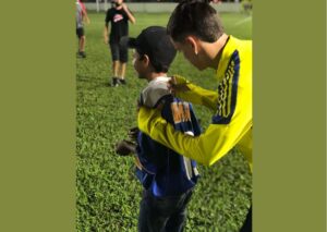 Imagem de um jovem autografando a camisa de uma criança.